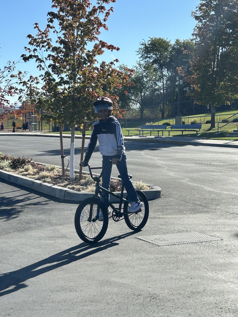 A boy standing on his bike pedals as he rolls through the school parking lot.