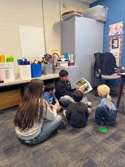 A boy reads his book to a group of elementary students.