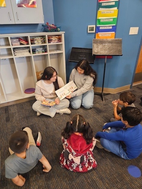 Two middle school girls read a book they created to elementary students.