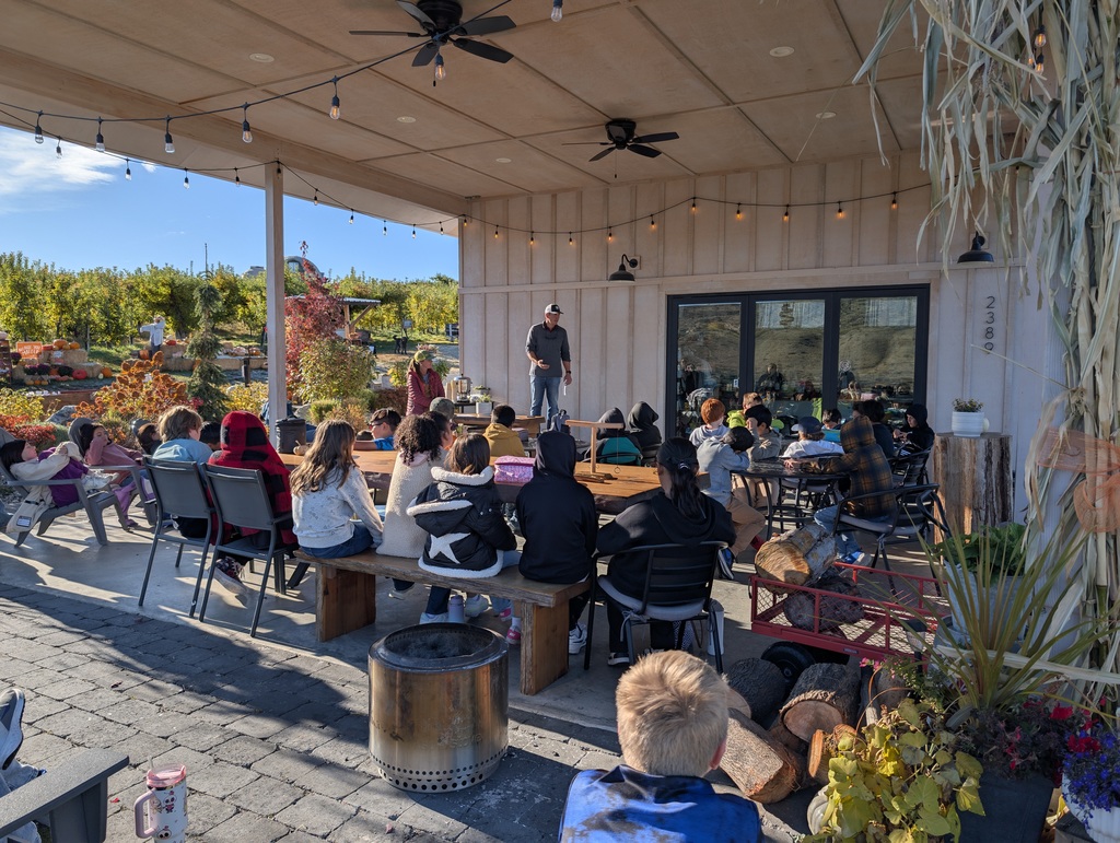 Farmer talks to students while they sit at picnic tables.