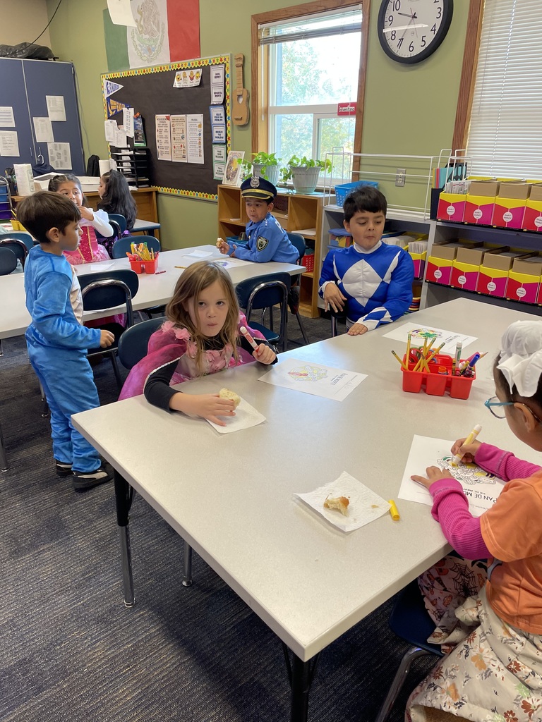 A classroom full of kids in Halloween costumes enjoy pan de muerto.