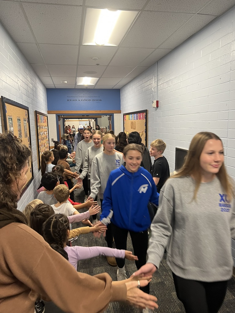Girls cross country team, high fiving elementary students in the hall.