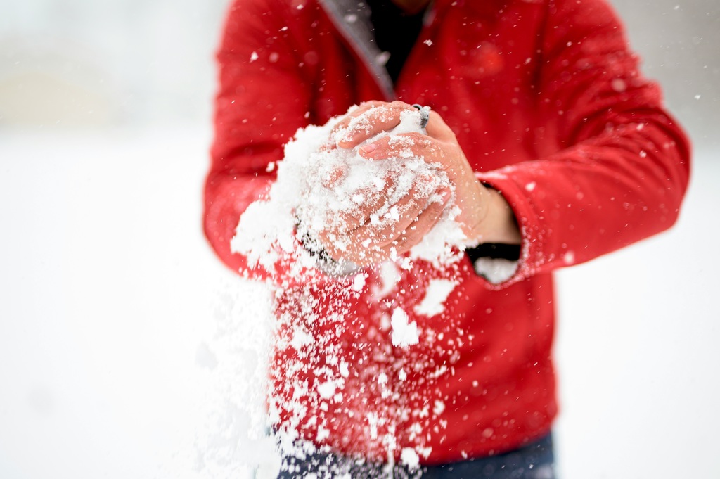 Man in a red coat making a snowball.