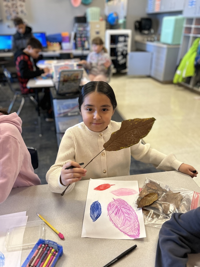 Third grade student holds a leaf above her drawing of fall leaves.