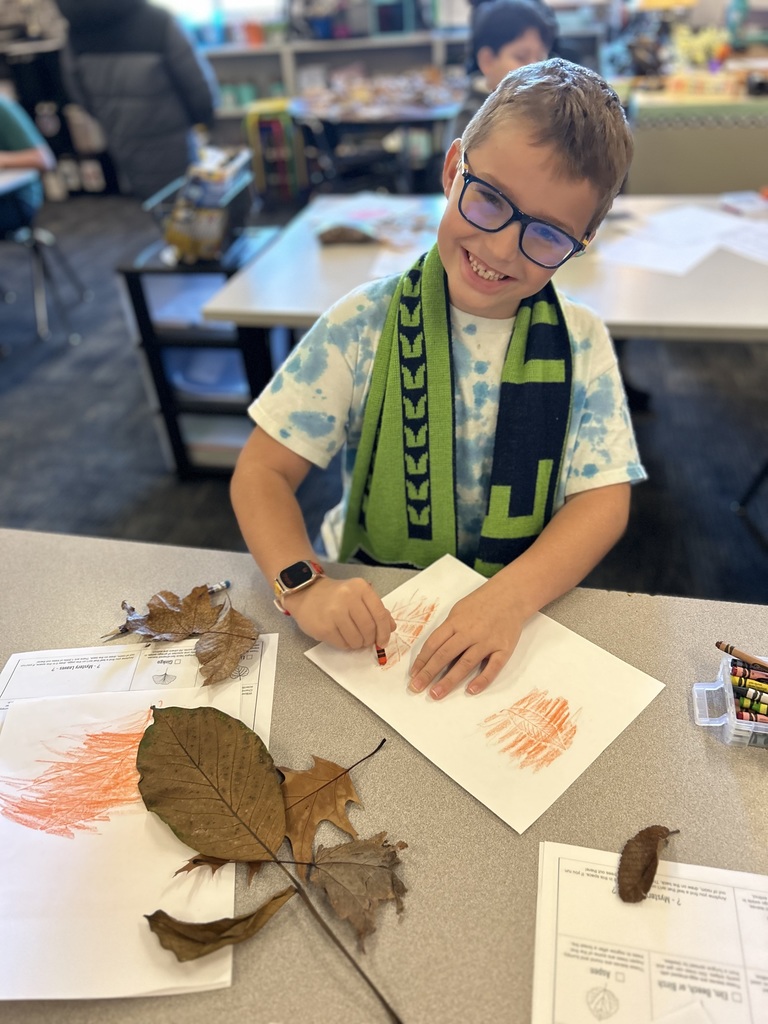 A boy uses an orange crayon to trace leaves.