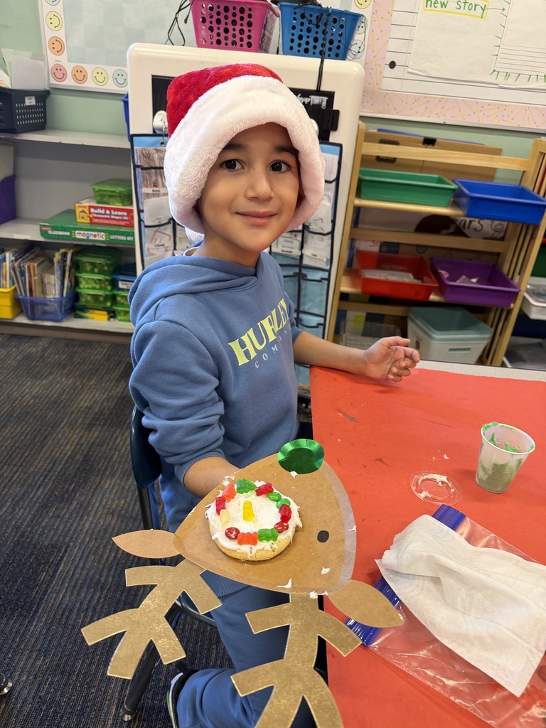 A boy in a Santa hat shows a decorated cookie on top of a reindeer cutout.