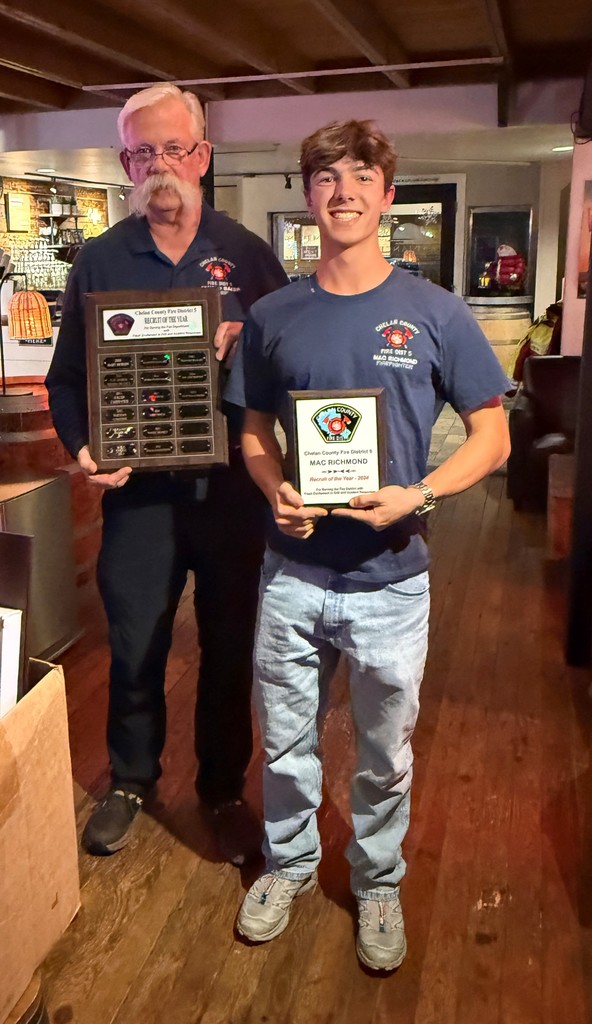 Fire chief and recruit stand holding plaques.