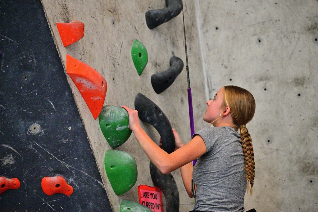 Teenaged girl on a gray shirt climbs a rock wall.