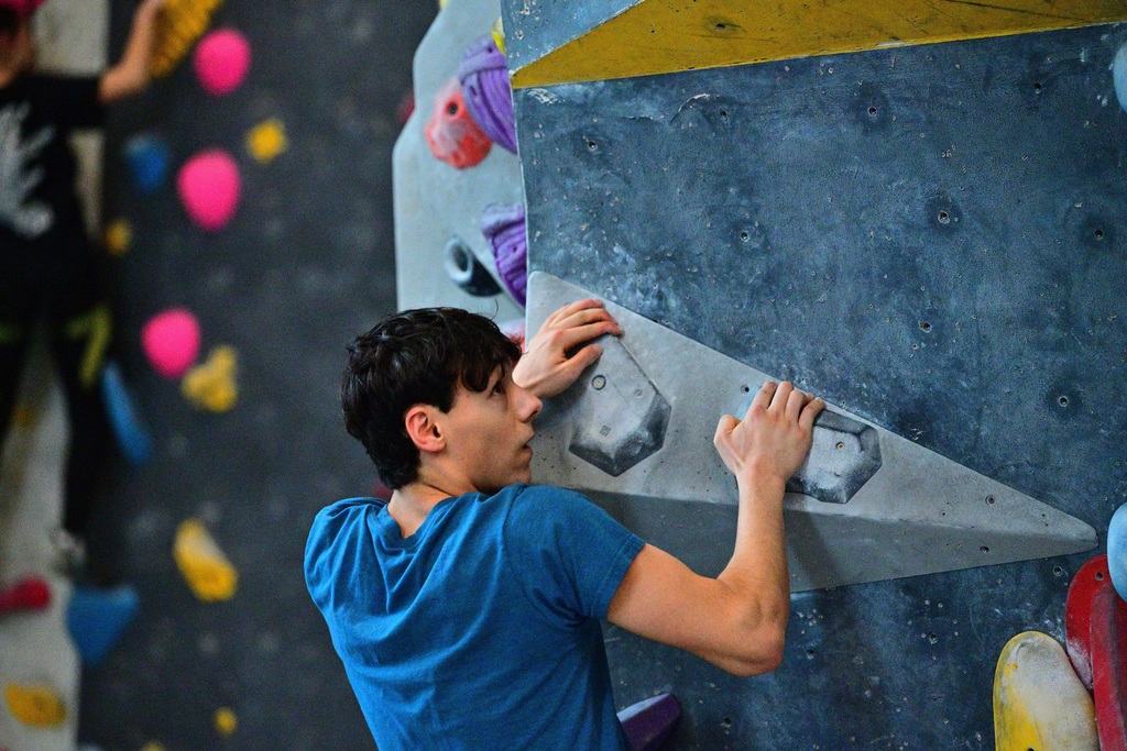 Teen boy in blue shirt climbs rock wall.