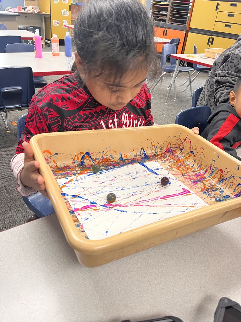 Students rolling marbles covered in paints around on paper.