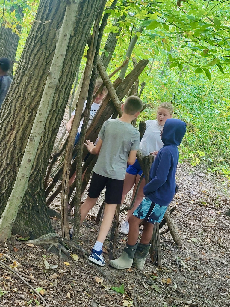 Students building a shelter out of wood in a forest at camp