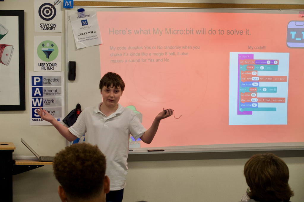 Student with shoulders shrugged explaining project to classmates.