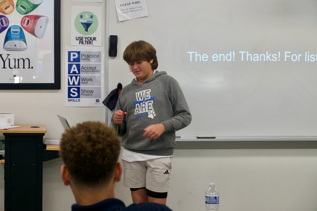 Male student showing a micro bot with a presentation behind him saying The End