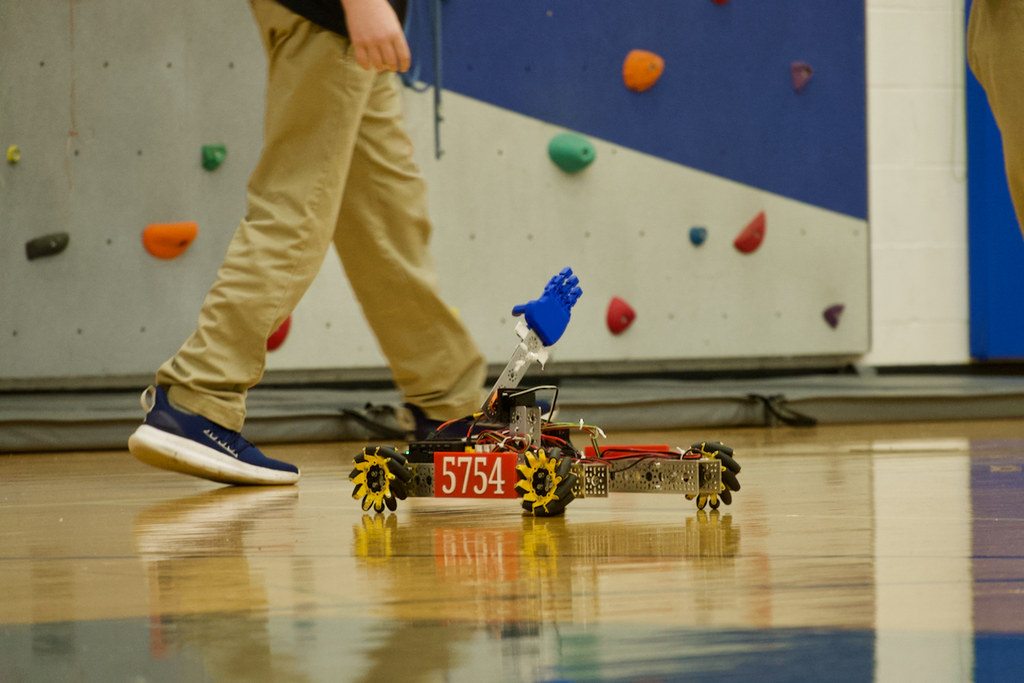 Robot on wheel with hand on the gym floor at Marburn Academy. A student is walking behind the robot.