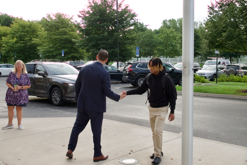 head of school shaking hands with a student entering the building