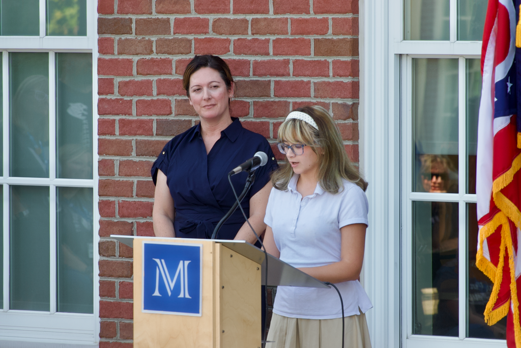 Student speaking at convocation while Associate Head of School Stephanie Royal looks on
