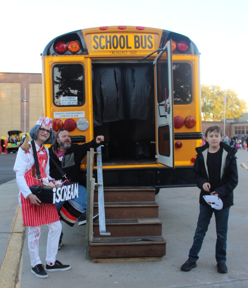 Students dressed in HAlloween costumes in front of haunted school bus