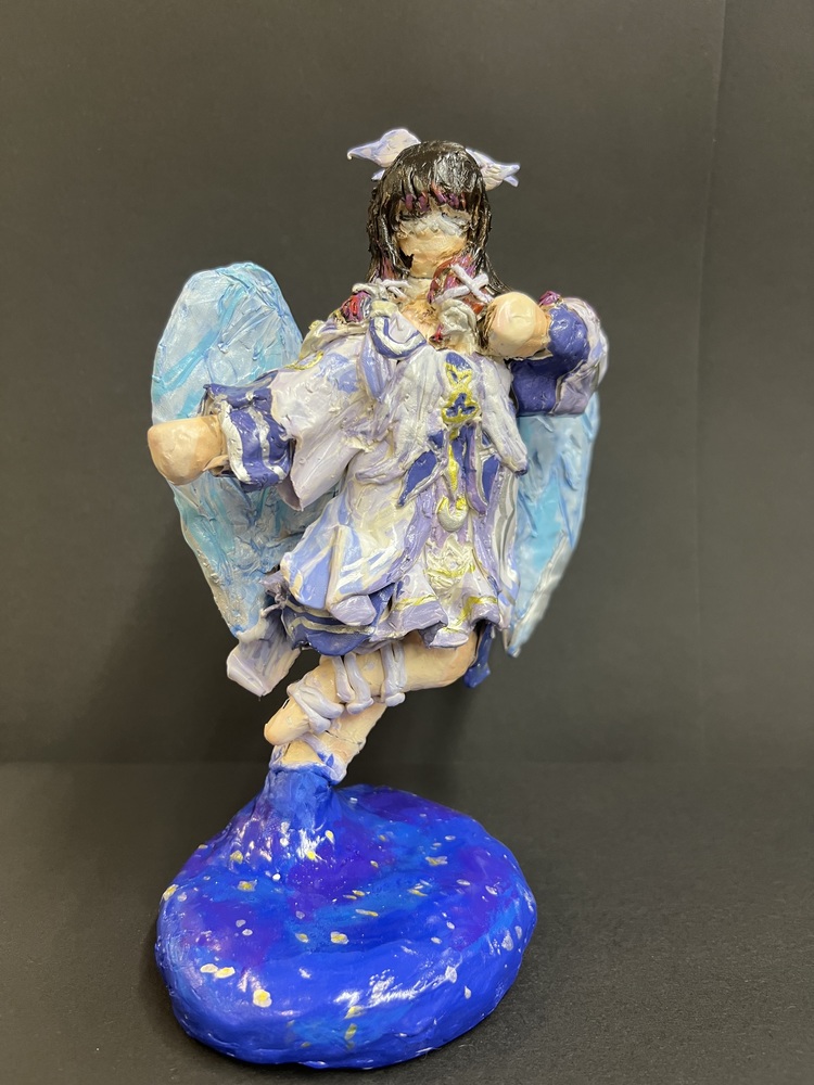 A handmade angel sculpture with blue wings, lavender clothing, and a galaxy-inspired base.