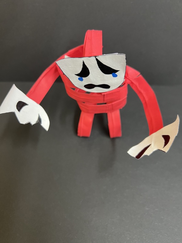 Red Paper Figure – Top View: An overhead view of the handmade red paper figure showing its curled body and emotional expression.