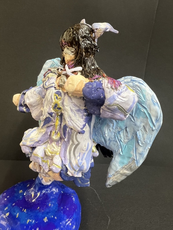 A side view of a detailed angel sculpture with flowing robes and textured blue wings.