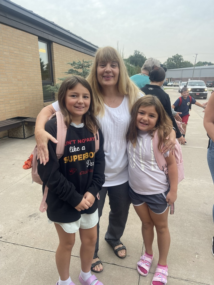 A grandma who is greeting students stops and takes a picture with her two granddaughters 