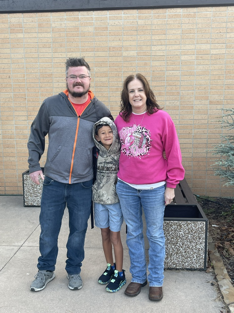 A MES students takes a picture with two greeters which are his mom and uncle