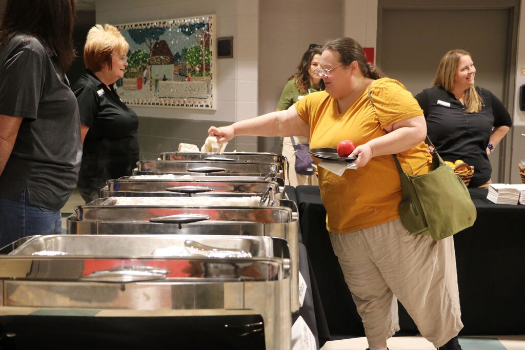 Staff member picks up a breakfast sandwich in the buffet line. 