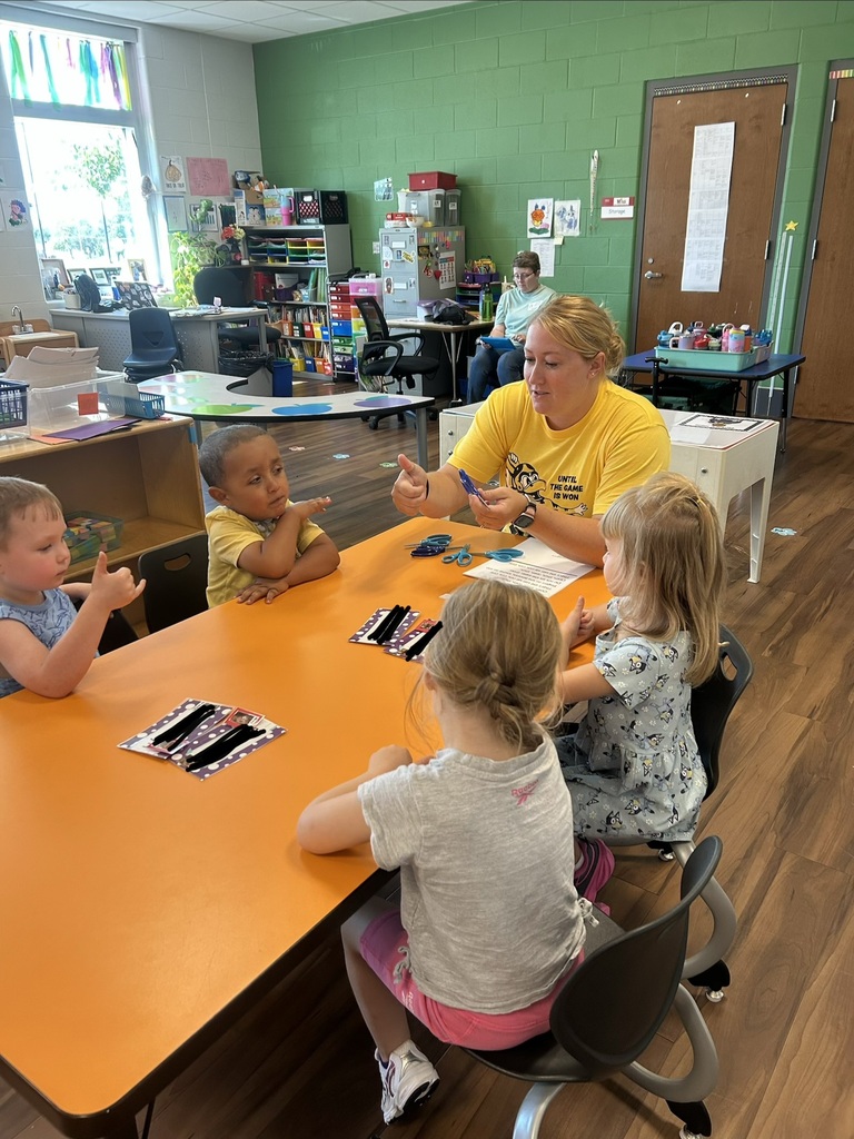 An associate helps four students learn how to use a pair of scissors at a table. 