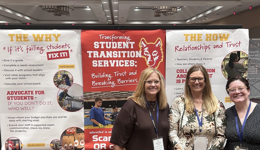 A group of three presenters stand in front of their display at the DCDT Conference.