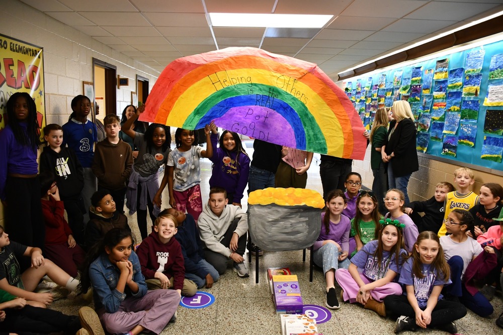 students holding up a giant paper rainbow and smiling