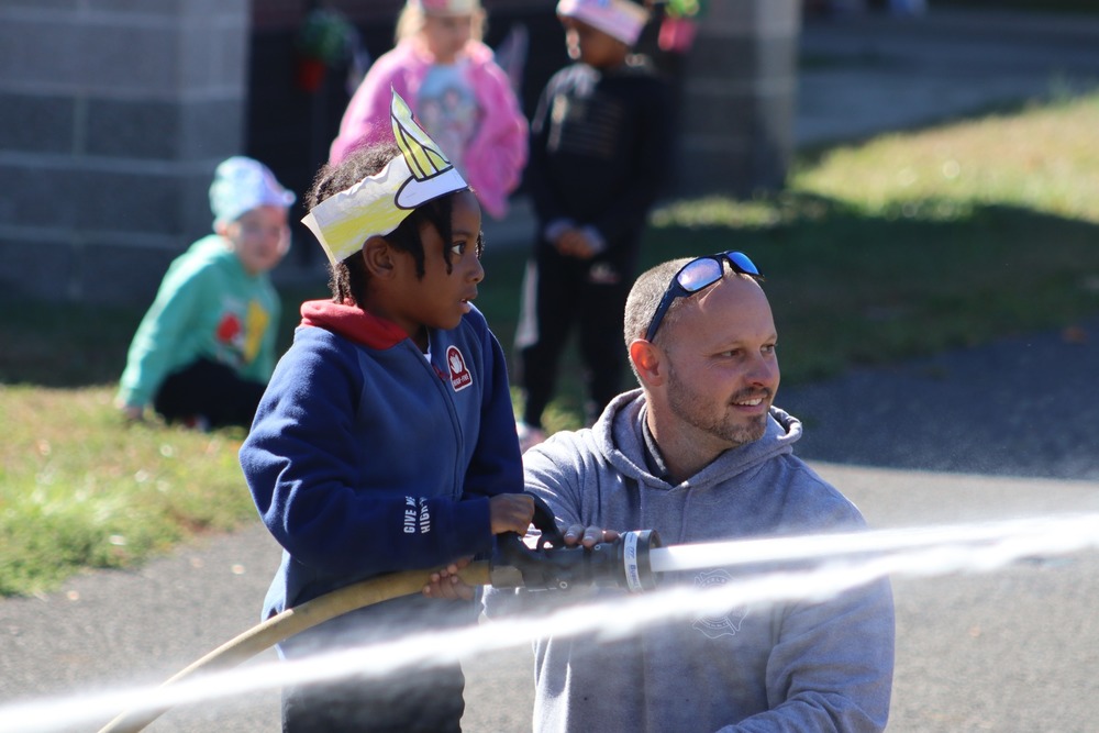 A student holds a fire hose as a firefighter looks on