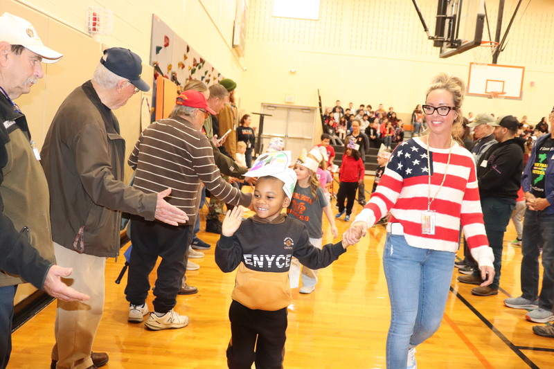 A student waves to a line of veterans