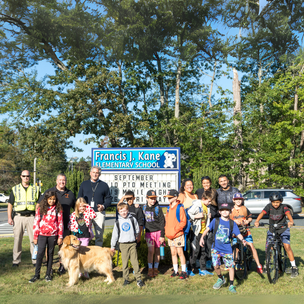 Kane School Assistant Principal, Marlborough Police Department staff members, students, and family members pose for a group photo outside in front of the Kane School sign after walking during a Fitness Friday event.