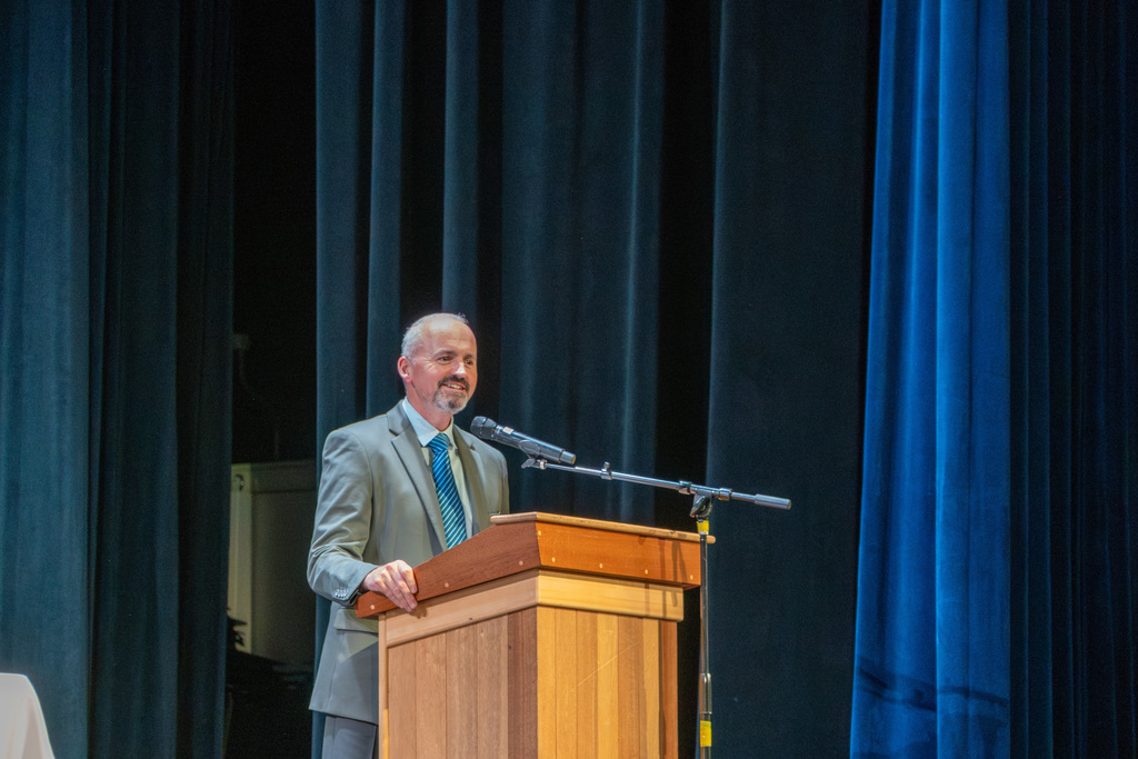  Interim Superintendent Jason DeFalco smiles as he stands at a podium.