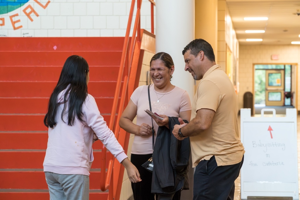 A student and two adults stand talking and smiling near a flight of stairs.
