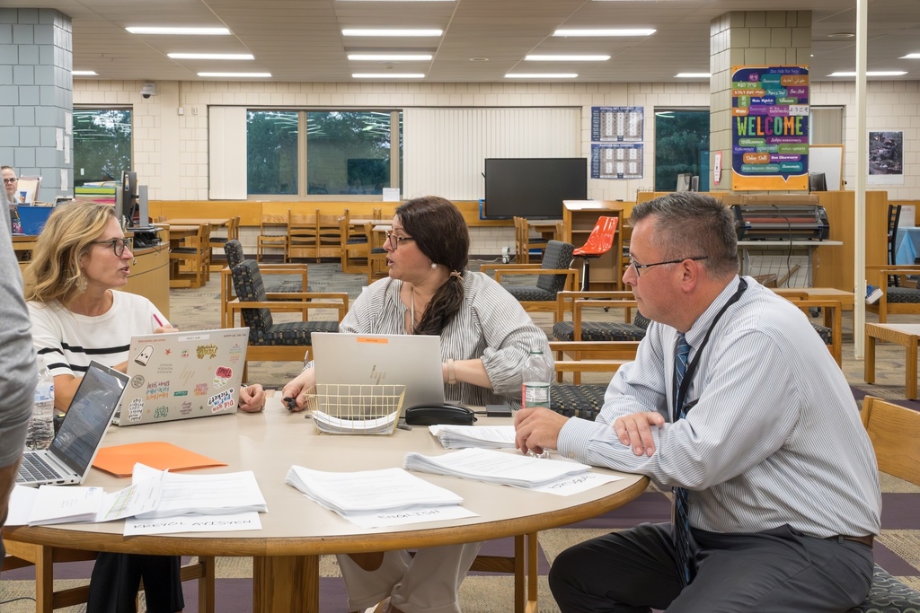 MHS Principal Stephen Sierpina sits at a table with two staff members inside the MHS library.