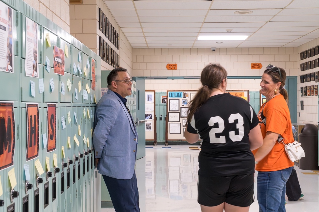 An MHS staff member stands in a hallway talking to a student and her mother.