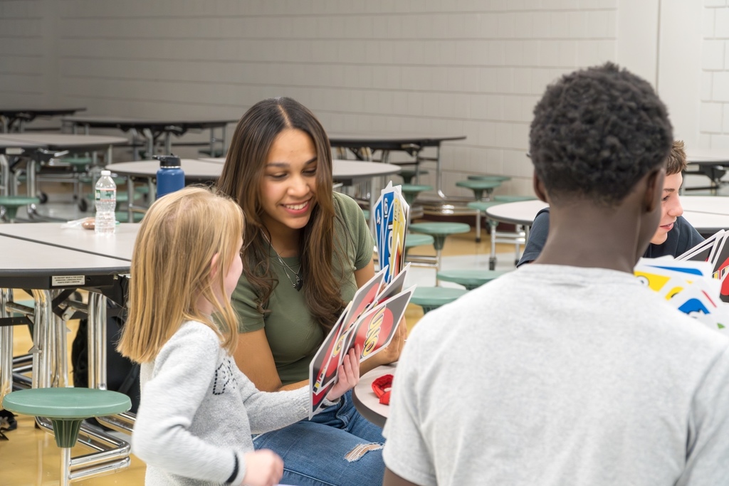 An MHS student helps a young girl play Uno with a group of students in the MHS cafeteria.