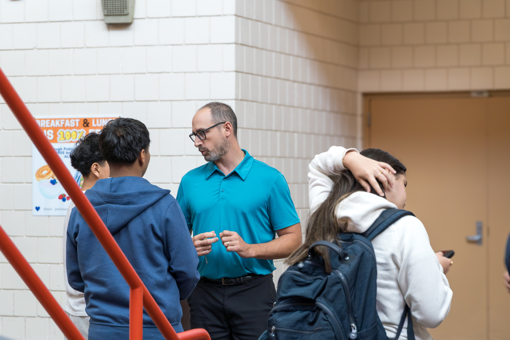 An MHS employee stands and talks with two students.