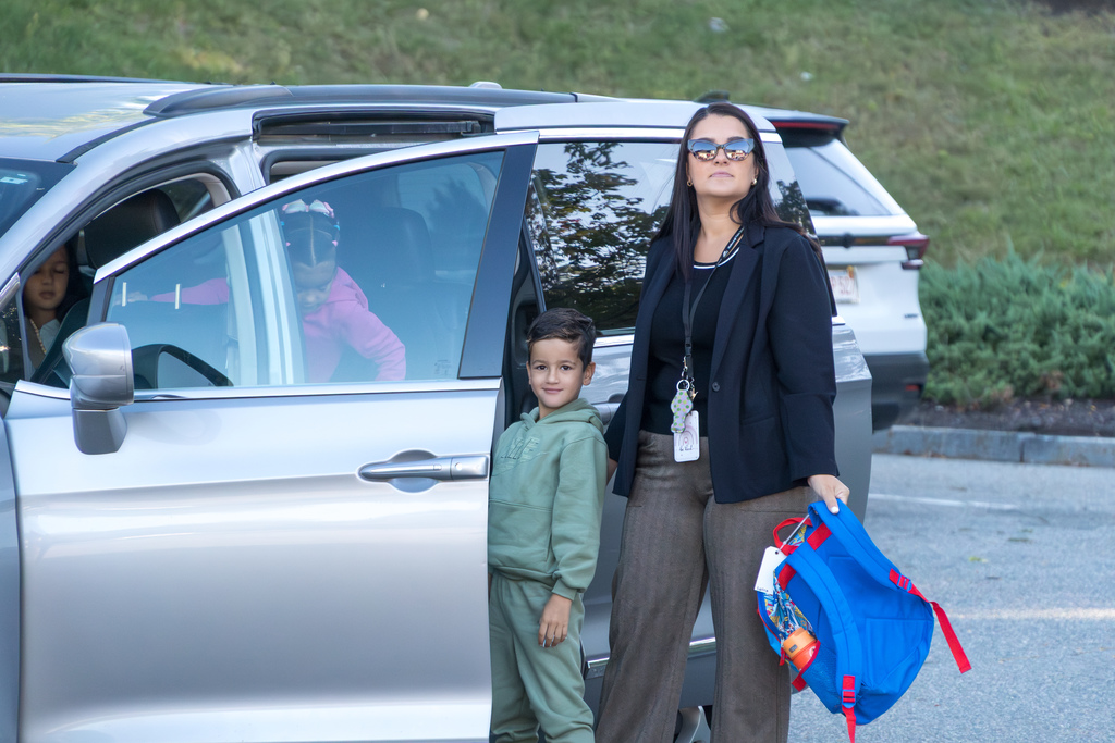 A Richer School student stands and smiles next to a minivan. A family member stands next to him, holding his backpack.