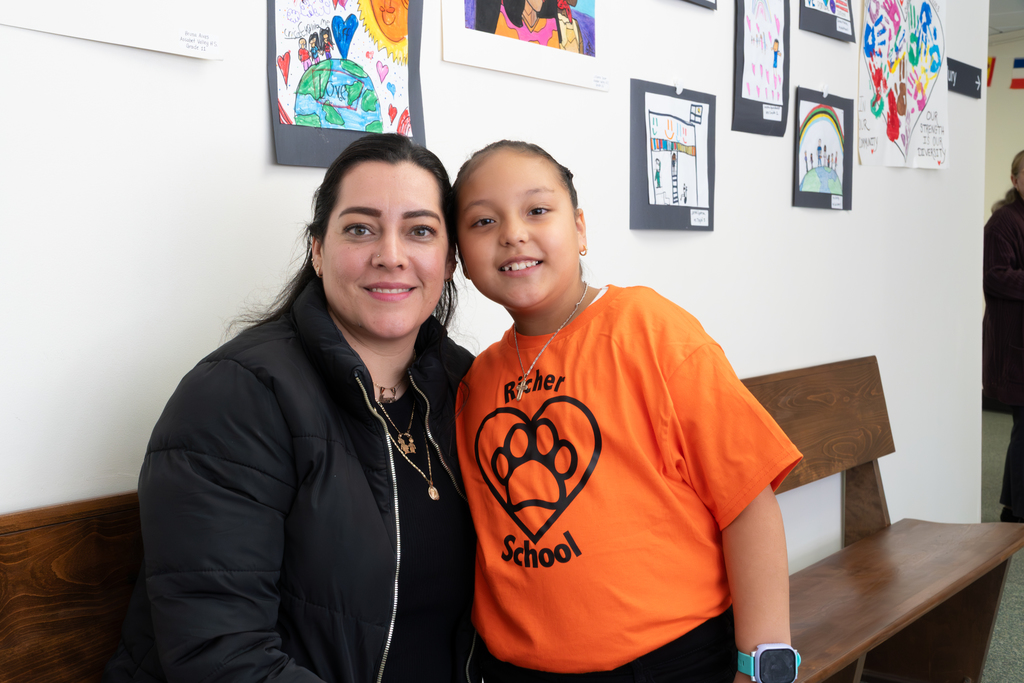 A student wearing an orange Richer School shirt and her mother pose for a photo.
