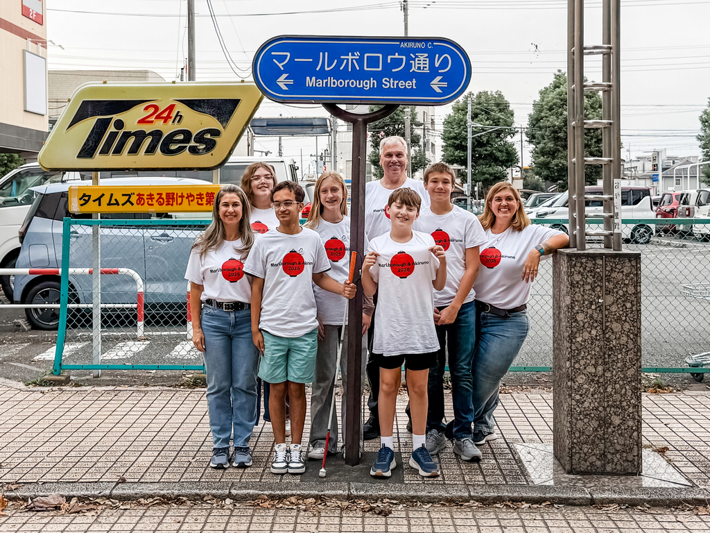 Five Whitcomb students and three staff members pose for a group photo in front of the "Marlborough Street" sign in Japan.
