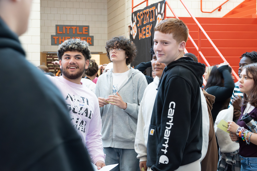 Three 8th-grade boys stand and smile in the middle of a crowd outside the MHS little theater.