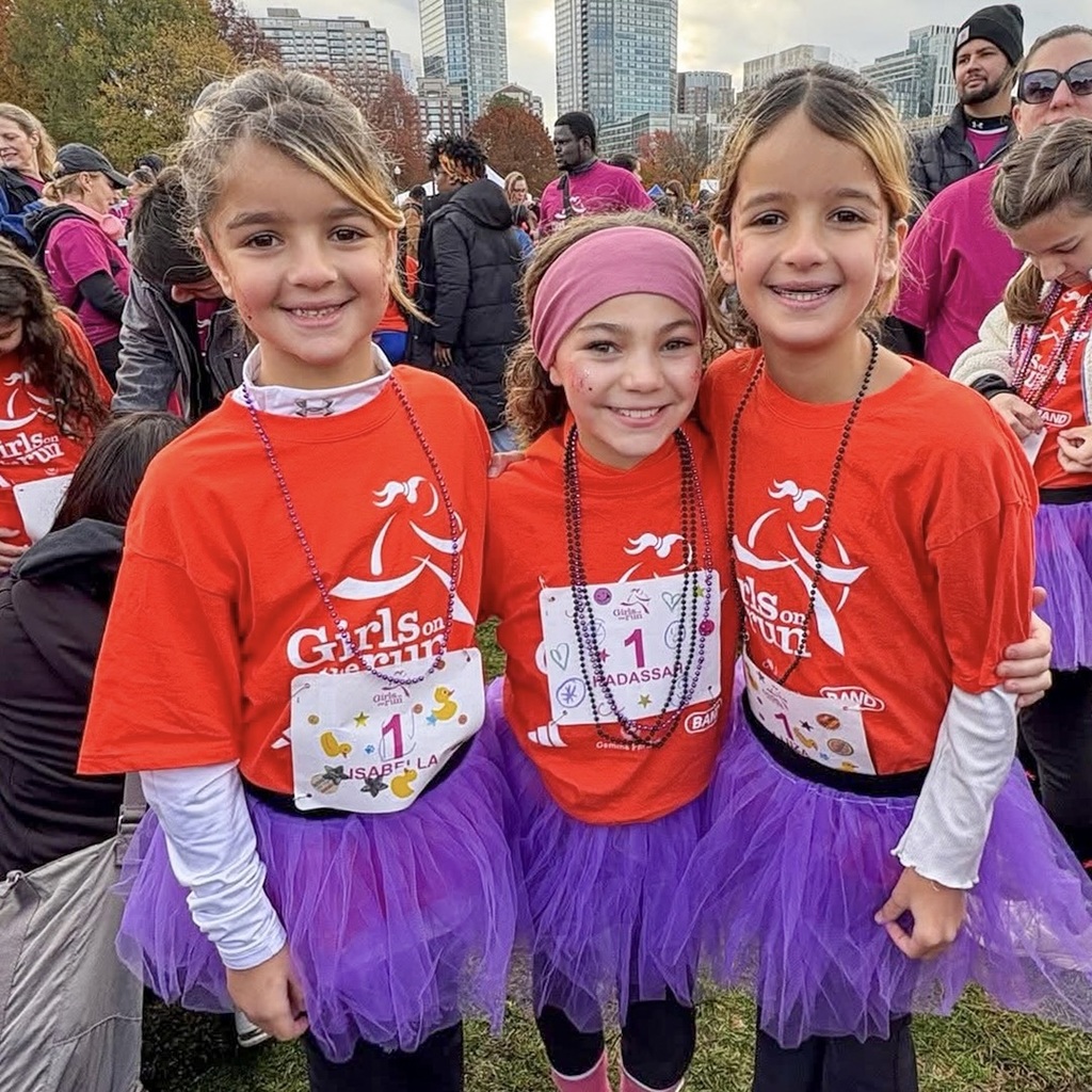 Three MPS female students wearing purple tutus and red Girls on the Run shirts and bibs pose for a photo.