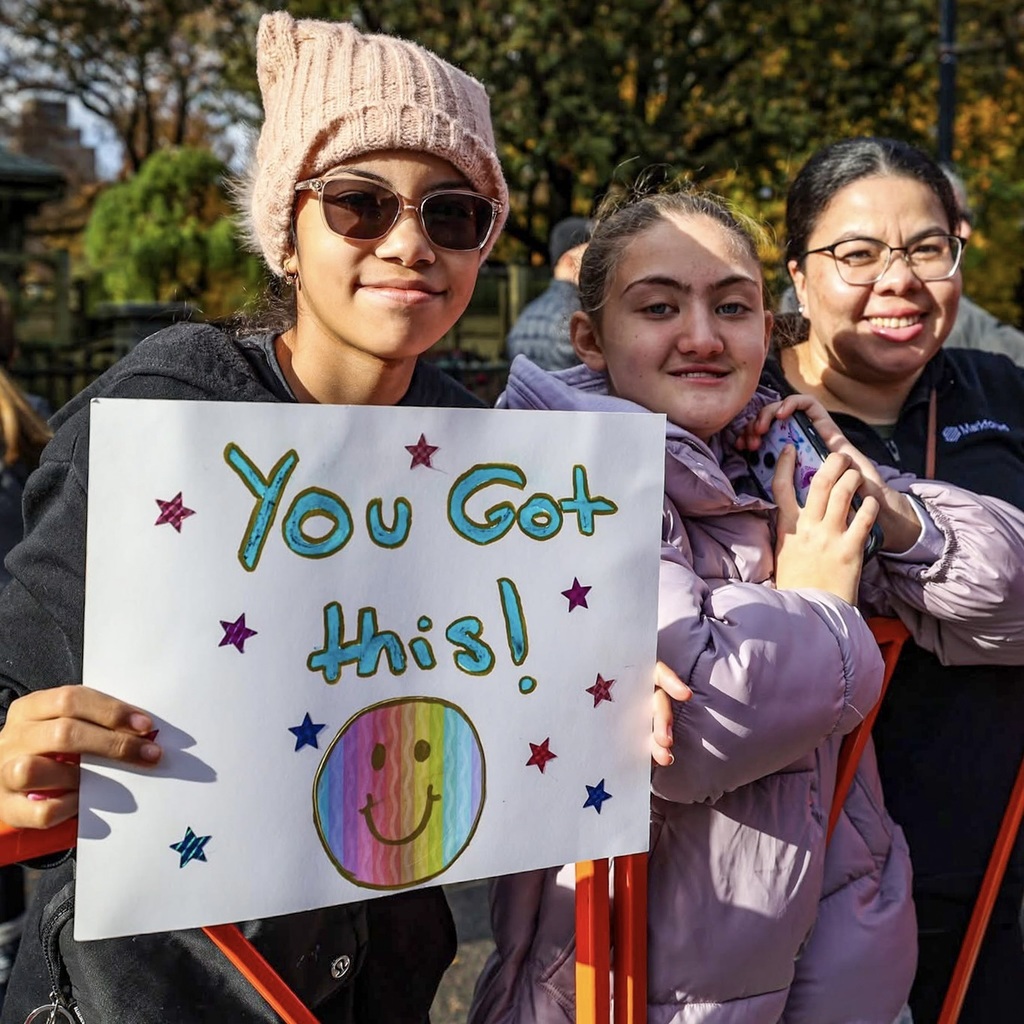 Three girls smile and pose for a group photo. One girl holds a sign that says "You got this!" with a smiley face.