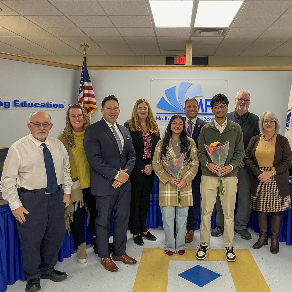  Two award-winning students, each holding a bouquet of flowers, stand for a group photo with the Marlborough School Committee.