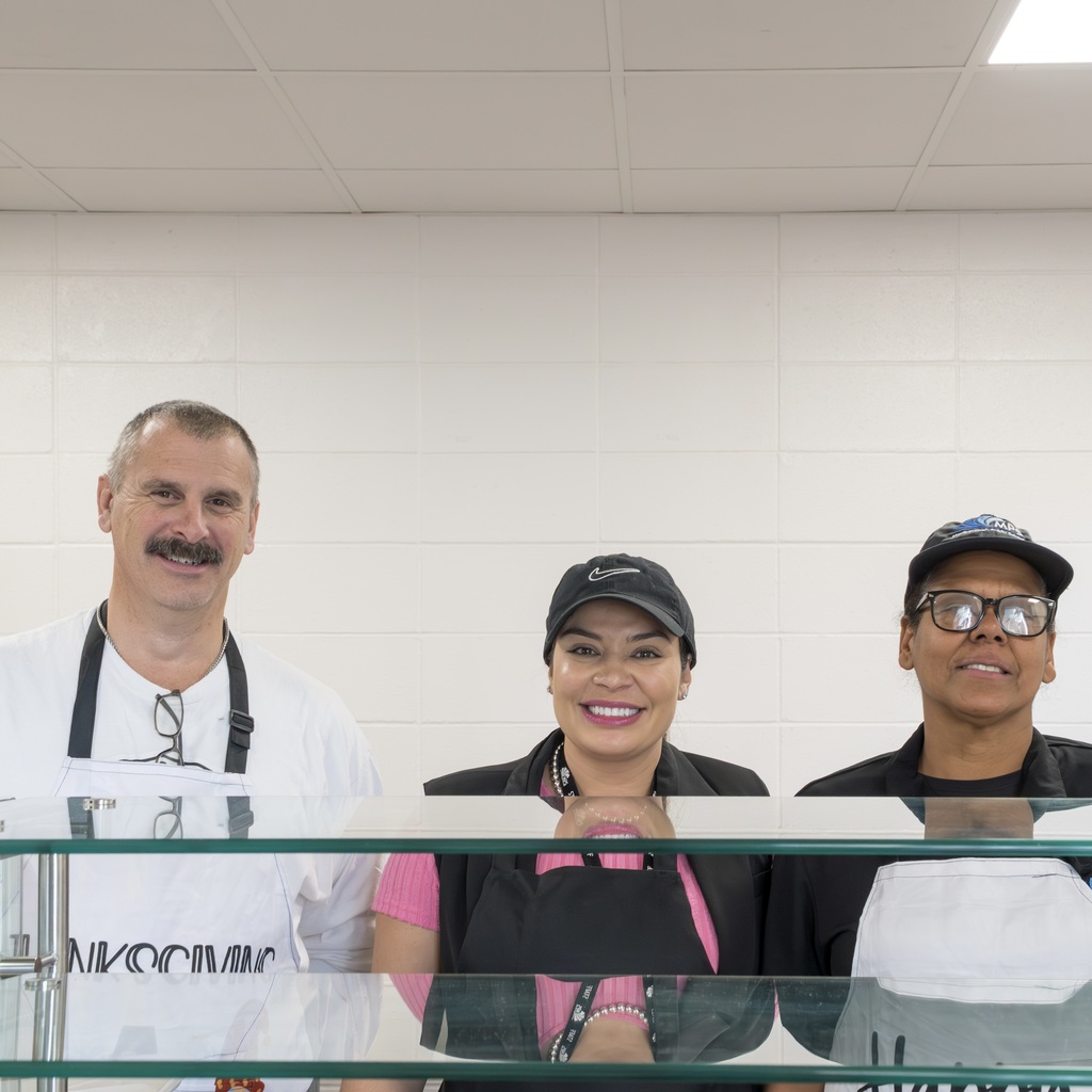 Three MPS staff members stand for a group photo behind the counter in the Whitcomb cafeteria.