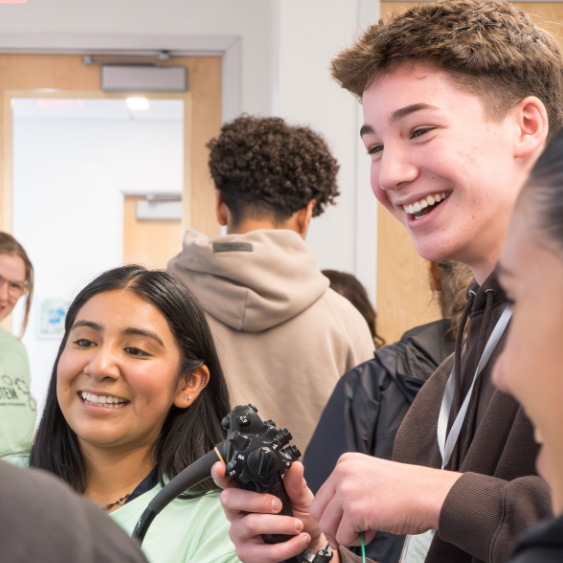 A smiling MHS student practices using a medical device with help from a Boston Scientific employee.