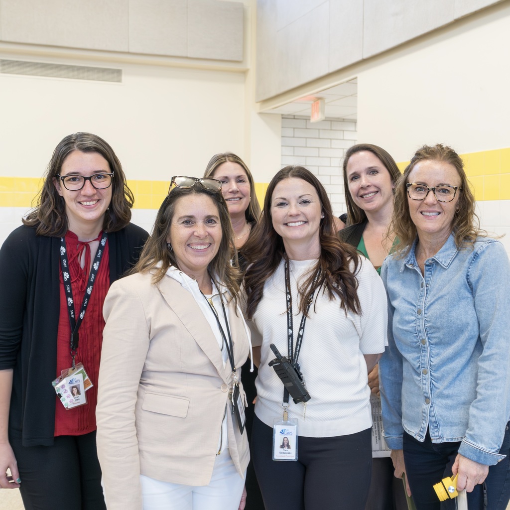 Six Whitcomb staff members smile and stand for a group photo in the cafeteria.