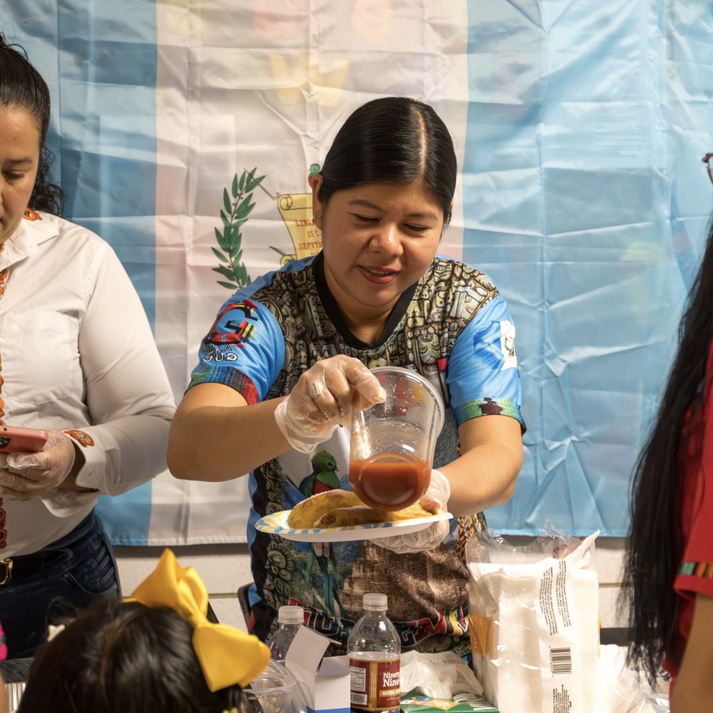 A Guatemalan mother pours a sauce onto a plate of food.